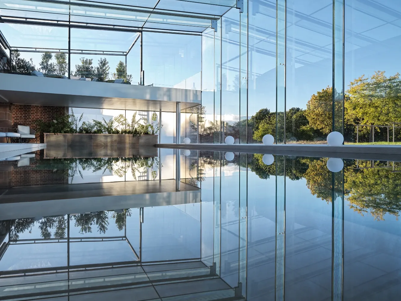 Frameless glass pool house reflected in a still outdoor swimming pool