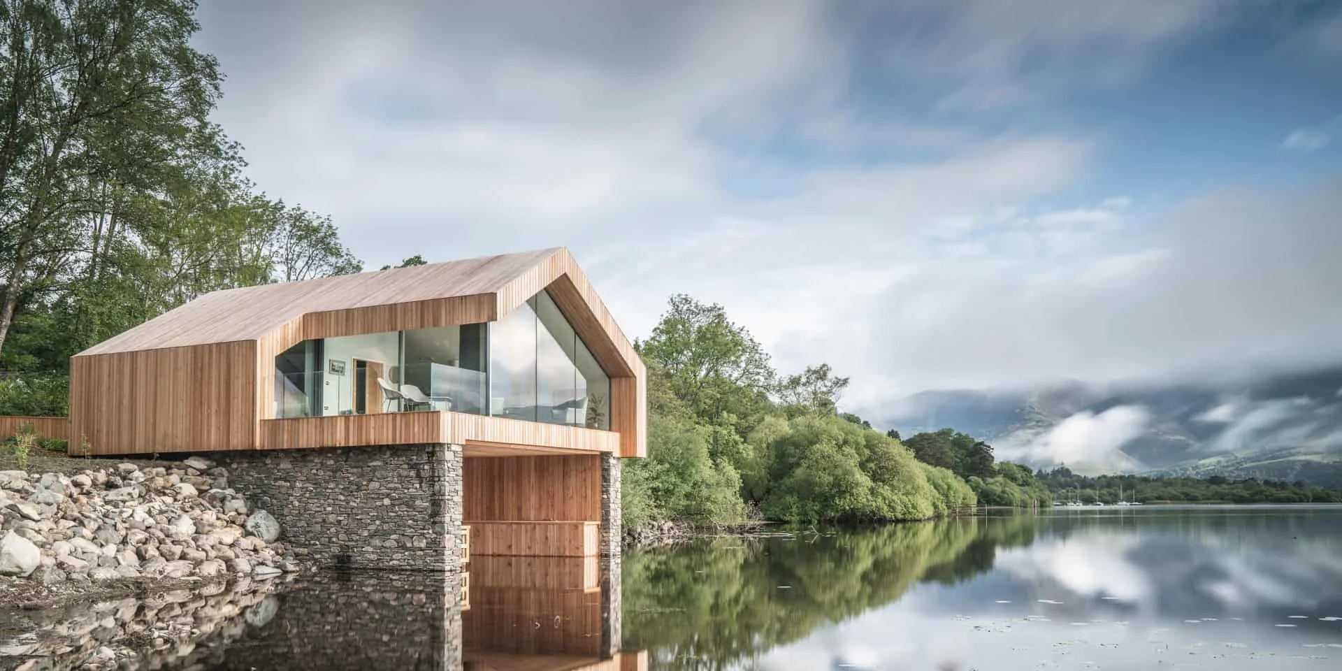 Timber-clad boathouse with a frameless glass gable, on the edge of a lake in the Lake District