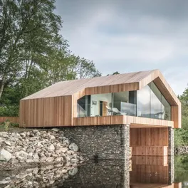 Timber-clad boathouse with a frameless glass gable, on the edge of a lake in the Lake District