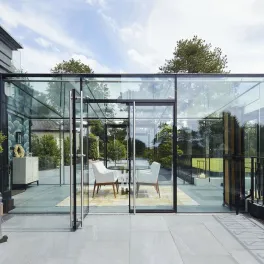Frameless Skyframe glass room at a house in Whitegate, Cheshire, with white dining chairs inside