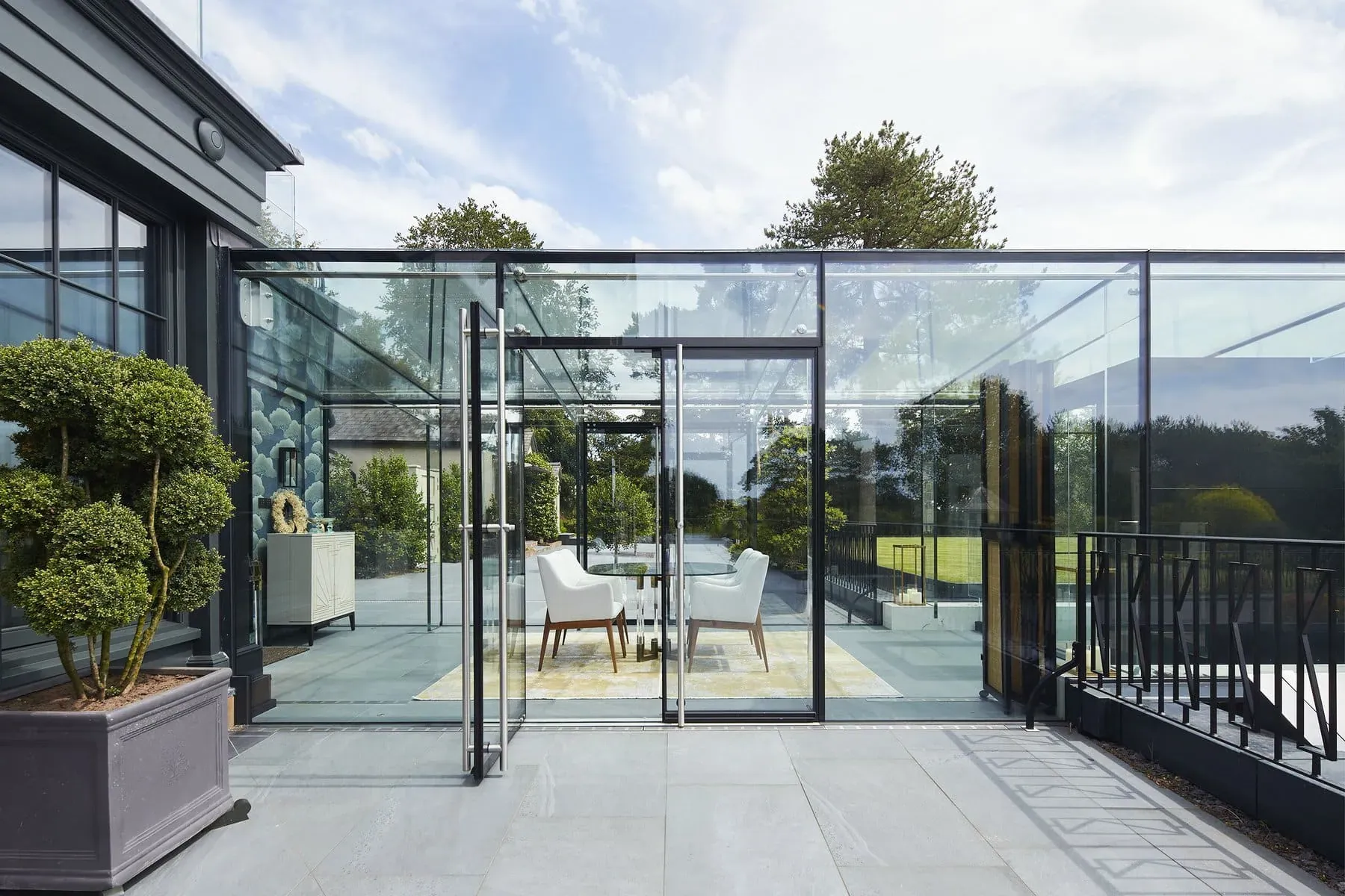 Frameless Skyframe glass room at a house in Whitegate, Cheshire, with white dining chairs inside